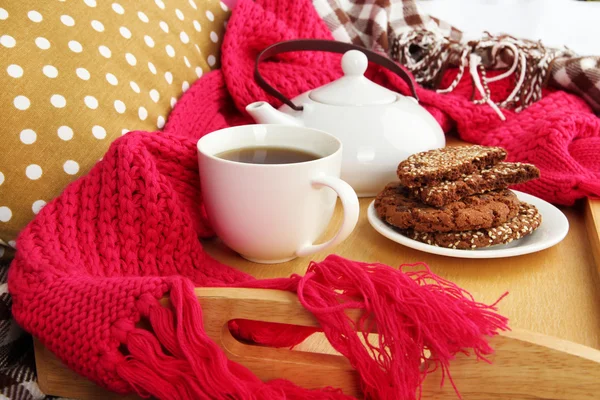 Cup and teapot with cookies on tray and scarf on bed close up — Stock Photo, Image