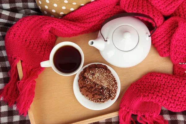 Cup and teapot with cookies on tray and scarf on bed close up — Stock Photo, Image