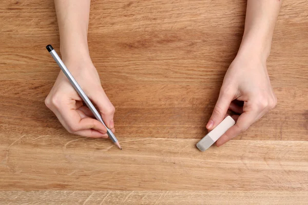 Mãos humanas com lápis e borracha apagada no fundo da mesa de madeira — Fotografia de Stock