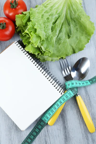 Couverts attachés avec ruban à mesurer et cahier avec légumes — Photo