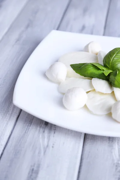 Sabroso queso mozzarella con albahaca en plato sobre fondo de madera — Foto de Stock