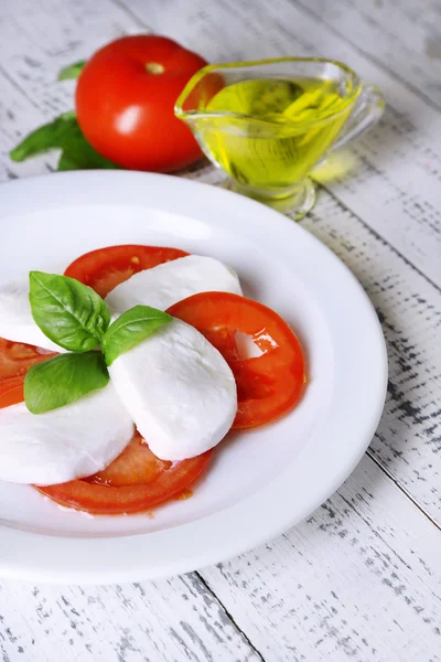 Caprese-Salat mit Mozarella, Tomaten und Basilikum auf Teller, auf Holztischhintergrund — Stockfoto