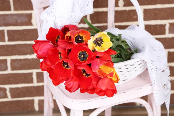 Strauß bunter Tulpen im Weidenkorb, auf Stuhl, auf dem heimischen Innenhintergrund — Stockfoto