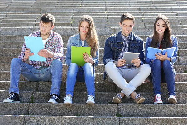 Happy students sitting on stairs in park