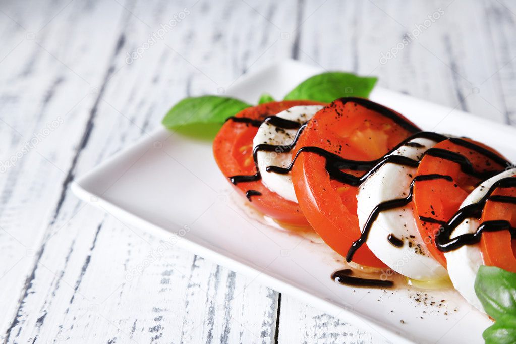 Caprese salad with mozarella cheese, tomatoes and basil on plate, on wooden table background