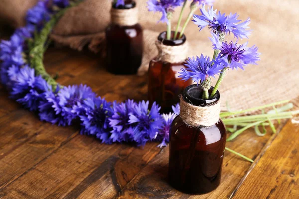 Beautiful cornflowers in glass bottles on wooden background — Stock Photo, Image