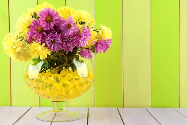Hermosas flores en jarrón con hidrogel sobre mesa sobre fondo de madera —  Fotos de Stock