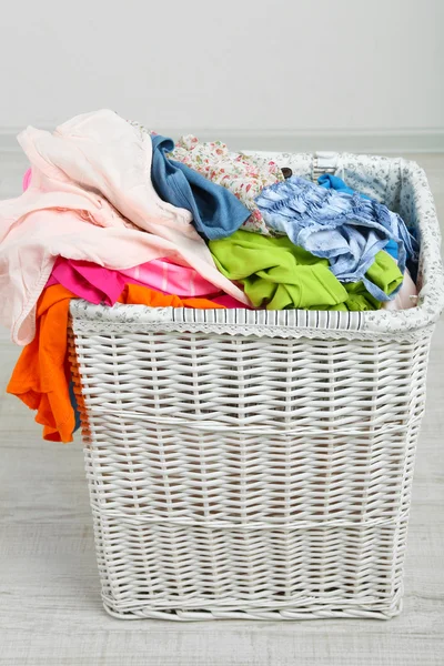 Full laundry basket  on wooden floor on gray background — Stock Photo, Image