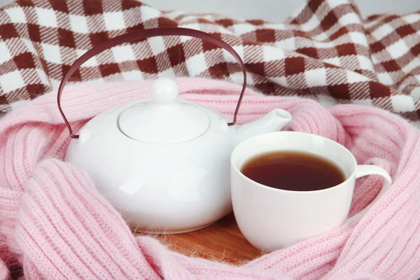 Cup and teapot on wooden stand and scarf on fabric background — Stock Photo, Image