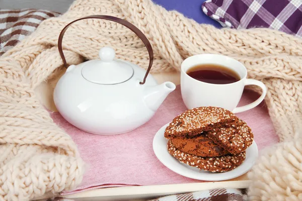Taza y tetera con galletas en bandeja y bufanda en la cama de cerca — Foto de Stock