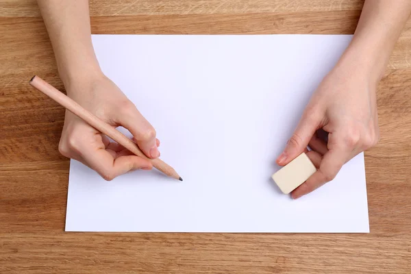 Manos humanas con lápiz escrito sobre papel y goma de borrar sobre fondo de mesa de madera — Foto de Stock