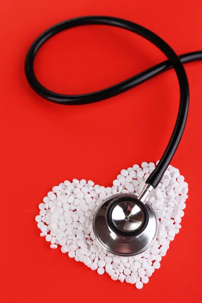 Serce stetoskop na czerwonym tle i pigułki — Zdjęcie stockowe