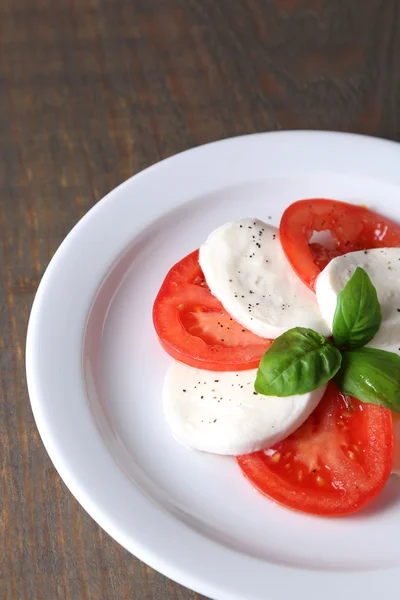 Caprese salad with mozarella cheese, tomatoes and basil on plates, on wooden table background — Stock Photo, Image