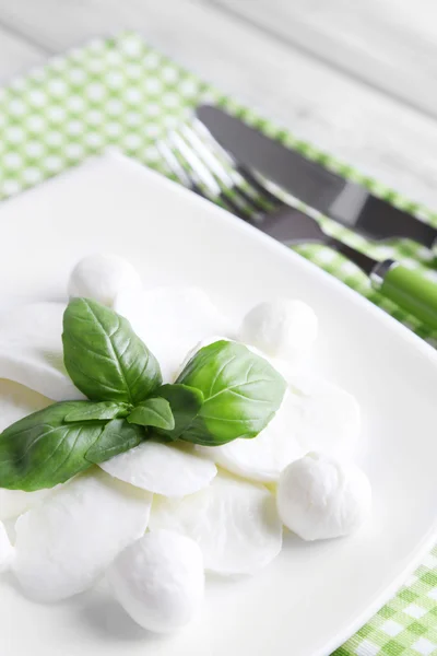 Schmackhafter Mozzarella-Käse mit Basilikum auf Teller auf Holzgrund — Stockfoto