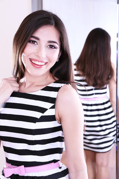 Beautiful girl trying dress near mirror in room — Stock Photo, Image