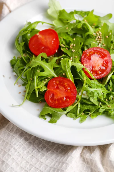 Grüner Salat mit Rucola, Tomaten und Sesam auf Teller, auf Holzgrund — Stockfoto