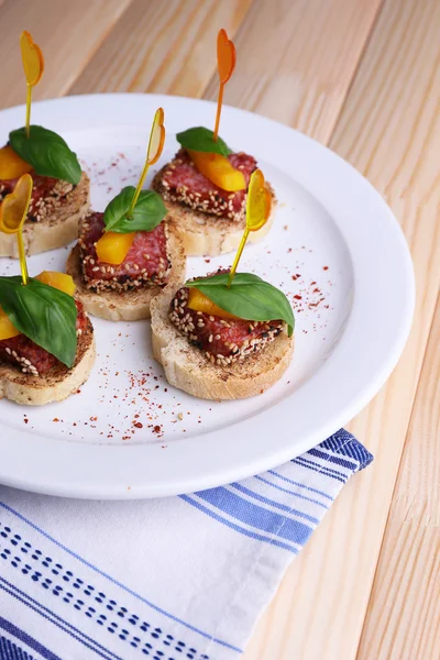 Gustose tartine con salame, pepe e foglie di basilico, su piatto, su fondo di legno — Foto Stock