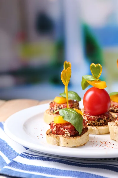 Välsmakande kanapéer med salami, tomat, paprika och basilika blad, på plattan, träbord, på ljus bakgrund — Stockfoto