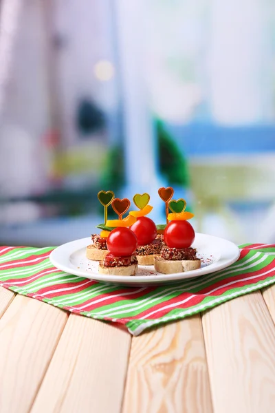 Välsmakande kanapéer med salami, tomat, paprika och basilika blad, på plattan, träbord, på ljus bakgrund — Stockfoto