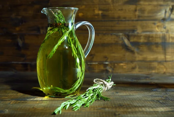 Essential Oil with rosemary in glass jug, on wooden background — Stock Photo, Image