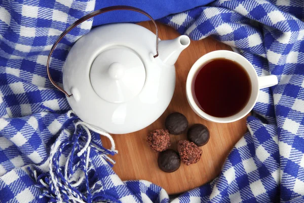 Cup en theepot met snoepjes op houten voet op stof achtergrond — Stockfoto