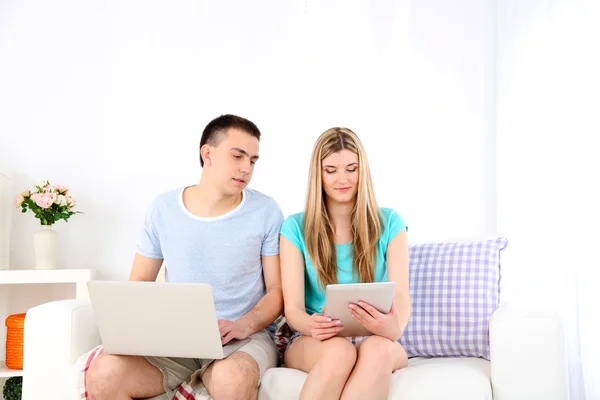 Liefdevol paar ontspannen met laptop en tablet, op huis interieur achtergrond — Stockfoto