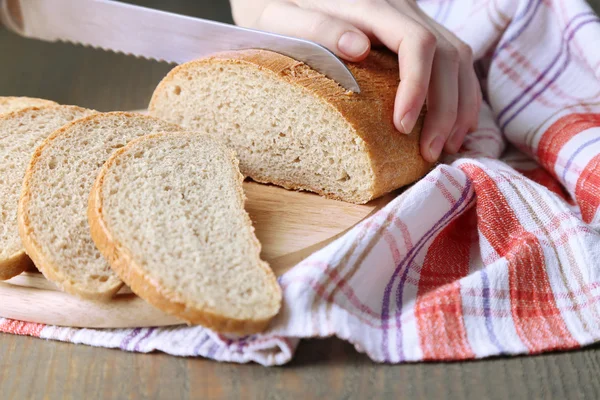 Mani femminili taglio del pane su tavola di legno, primo piano — Foto Stock