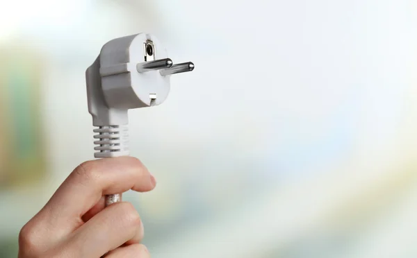 Hand holding electric plug on light background — Stock Photo, Image