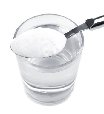 Spoon of baking soda over glass of water, isolated on white clipart