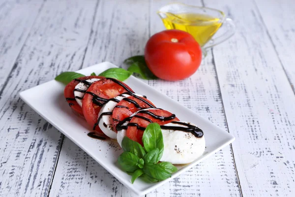 Salada Caprese com queijo mozarella, tomate e manjericão em prato, sobre fundo de mesa de madeira — Fotografia de Stock