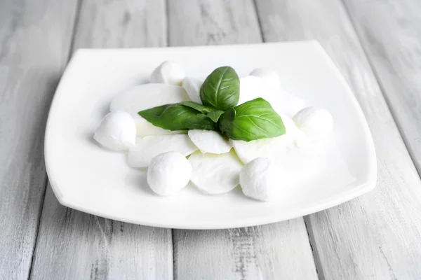 Sabroso queso mozzarella con albahaca en plato sobre fondo de madera — Foto de Stock