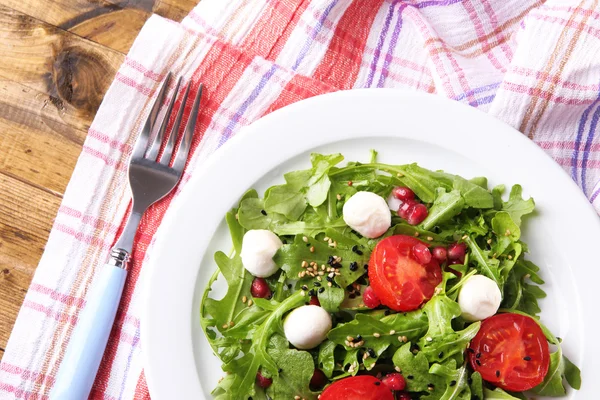 Ensalada verde hecha con rúcula, tomates, bolas de queso mozzarella y sésamo en plato, sobre fondo de madera — Foto de Stock