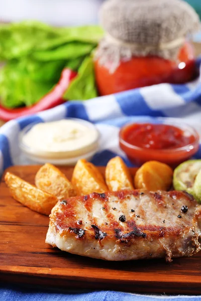 Gegrilltes Steak, gegrilltes Gemüse und gebratene Kartoffelstücke auf Holzbrett auf Tischhintergrund — Stockfoto