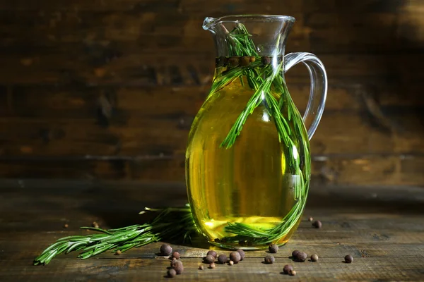 Olio essenziale con rosmarino in brocca di vetro, su fondo di legno — Foto Stock