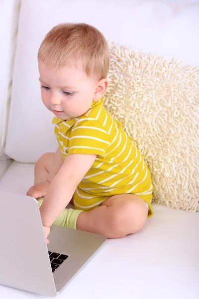 Lindo niño pequeño con portátil en el sofá en casa — Foto de Stock