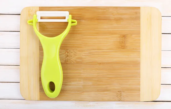 Eplucheur de légumes et planche à découper sur table en bois — Photo