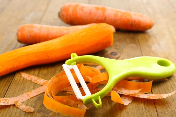 Carottes crues et éplucheur sur table en bois — Photo