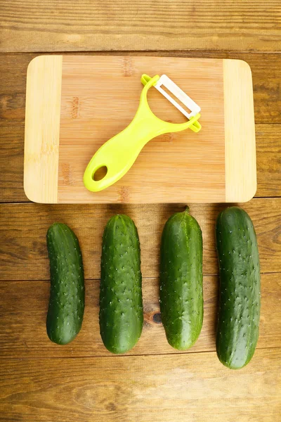 Peeler and cucumbers on wooden table — Stock Photo, Image