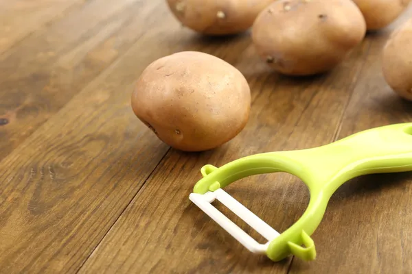 Peeler and potatoes on wooden table — Stock Photo, Image