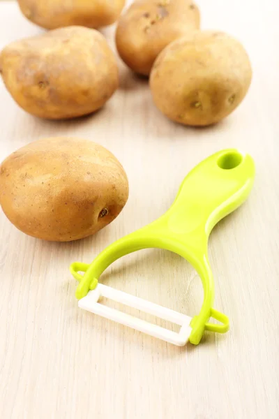 Peeler and potatoes on wooden table — Stock Photo, Image