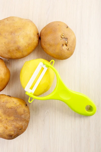 Peeler and potatoes on wooden table — Stock Photo, Image