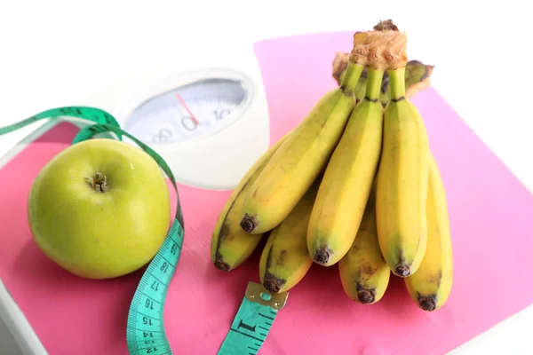 Bos van mini bananen en meetband op schalen, geïsoleerd op wit — Stockfoto