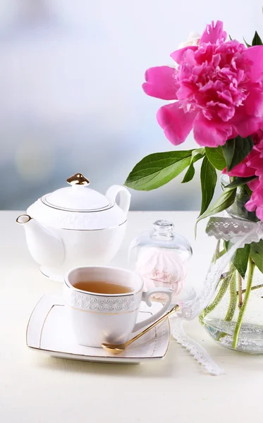 Σύνθεση πανέμορφο peonies στο βάζο, το τσάι στο φλιτζάνι και marshmallow, στο τραπέζι, επάνω ελαφρύς υπόβαθρο — Φωτογραφία Αρχείου
