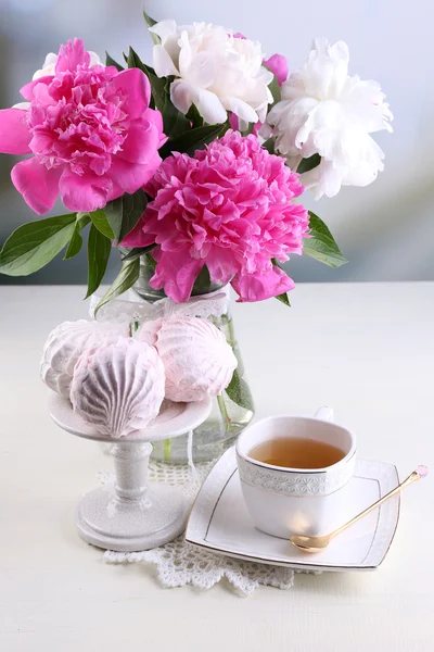 Composición de hermosas peonías en jarrón, té en taza y malvavisco, sobre mesa, sobre fondo claro —  Fotos de Stock