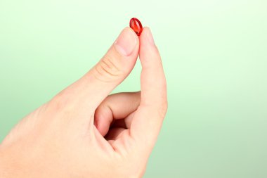 Kırmızı hapı yeşil arka plan yakın çekim tutan kadının el