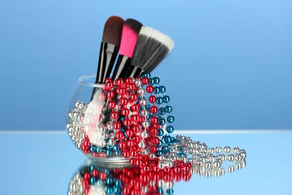 Pincéis de maquiagem em uma tigela com colar de pérolas no fundo azul — Fotografia de Stock