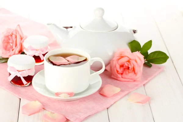Bule e xícara de chá com rosas e geléia na mesa de madeira branca — Fotografia de Stock