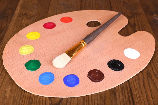 Wooden art palette with paint and brush on table close-up — Stock Photo, Image
