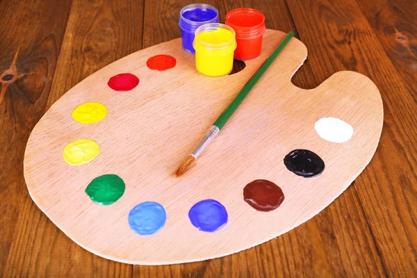 Wooden art palette with paint and brush on table close-up — Stock Photo, Image