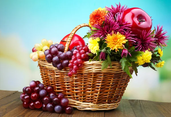 Komposition mit schönen Blumen in Weidenkorb und Früchten, auf hellem Hintergrund — Stockfoto